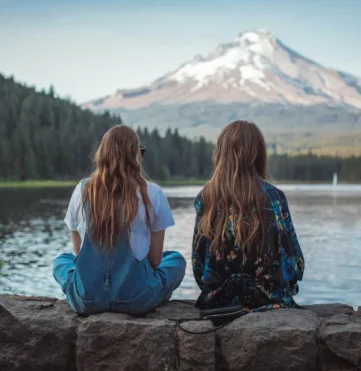 Two girls sitting on wall overlooking lake and mountains