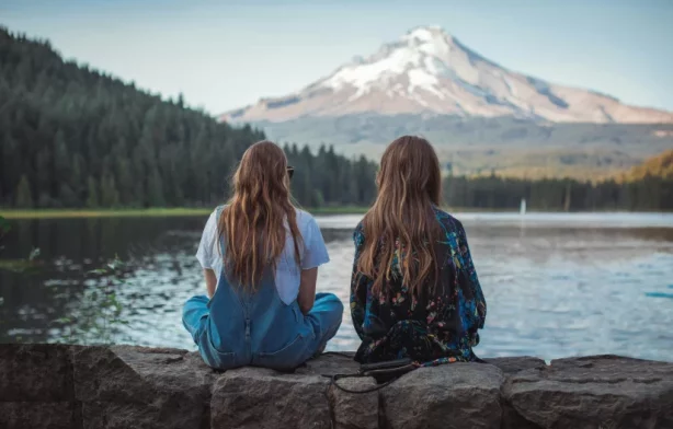 Two girls sitting on wall overlooking lake and mountains